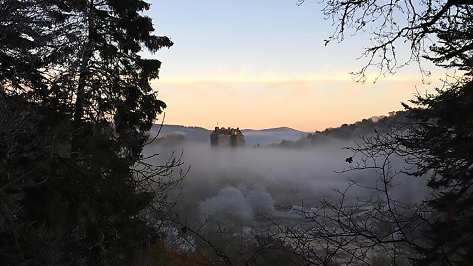 Mist-covered Neidpath Castle in Scotland viewed from the nearby forest on a crisp winter morning.